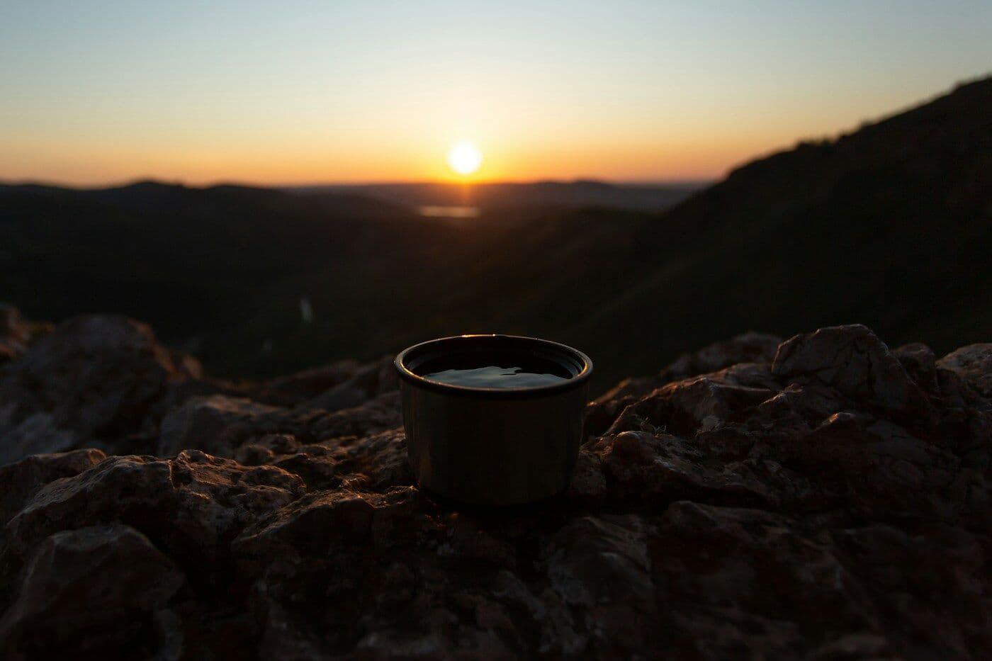 كوب قهوة على صخور الجبل وقت الغروب